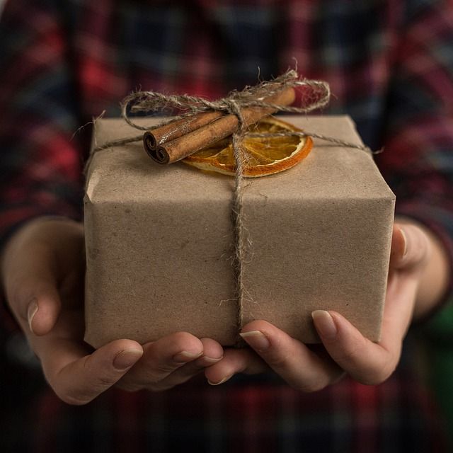 hands hold a box wrapped in brown paper with simple twine holding it together